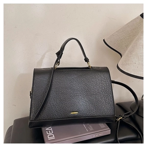 Détail du sac à main noir en cuir litchi avec un fermoir minimaliste en métal doré