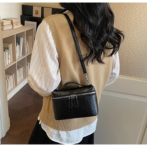 Detail of black ostrich leather texture and metal double zippers on crossbody bag
