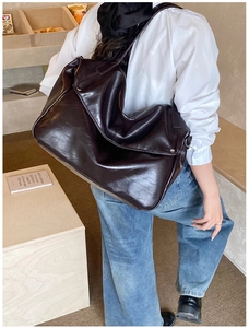 Detail einer großen braunen Kunstledertasche mit breitem Riemen und Silberschnalle am Model