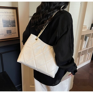 Detail of white quilted tote bag with gold chain strap in a premium home setting