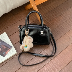 Détail du sac bandoulière en cuir verni noir avec bijoux argentés et breloque en peluche