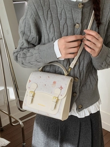 Cute cream cartoon bear handbag with bow patterns and gold hardware shown on a model