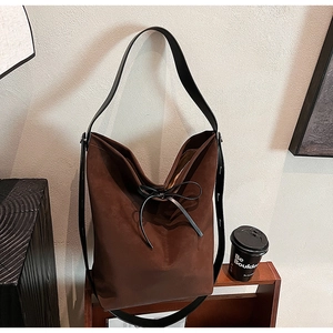 Detail of a brown suede tote bag featuring a leather tie bow and black long shoulder strap