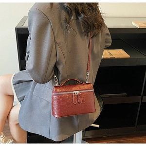 Detail of burgundy ostrich pattern box bag with silver hardware and top handle