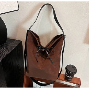 Close-up of brown suede bucket bag with a delicate leather bow and minimalist black strap