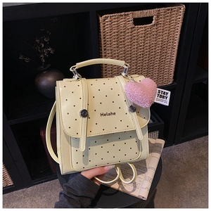 Close-up of cream polka dot backpack with decorative straps and pink plush heart charm