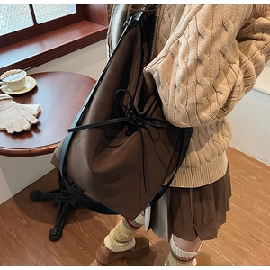 Brown leather tote bag featuring a black bow detail and slim shoulder straps in a cafe
