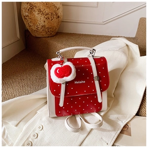Chic red polka dot backpack with plush cherry pendant and white straps on a beige suit
