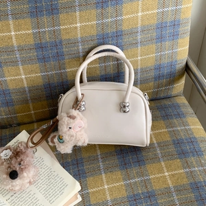 Gros plan du sac Boston crème avec détails argentés et charmant mouton en peluche