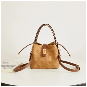 Close-up of embossed floral patterns and golden twist lock on dark camel bucket bag