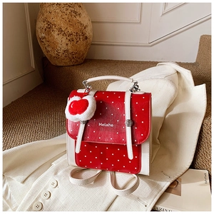 Detail of red polka dot backpack with white trim and heart-shaped plush keychain accessory