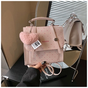 Detailed view of pink polka dot backpack featuring a heart charm and magnetic flap closure