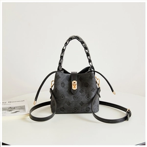 Detail of dark grey bucket bag with embossed patterns and woven handle on white table