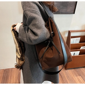 Detail of dark brown suede shoulder bag with black leather straps on a wooden shelf