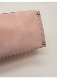 Detailed close-up of light pink textured leather with silver rivets and fine stitching