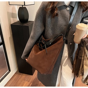 Brown suede tote bag for women with black leather wide strap and bow detail shown on shoulder