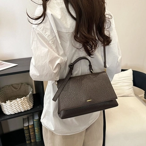Détail de la texture cuir litchi marron foncé sur un sac trapèze avec boucle métal
