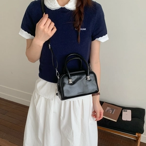 Détail d'un petit sac bandoulière noir brillant avec des éléments sphériques en métal