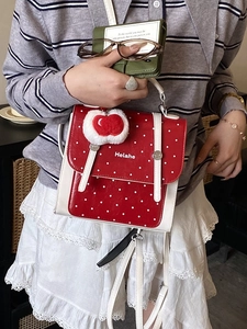 Retro red and white polka dot backpack with a plush apple charm and white top handle