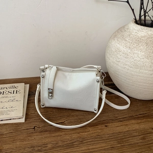 Detail of white textured leather crossbody bag with silver rivets on a wooden table