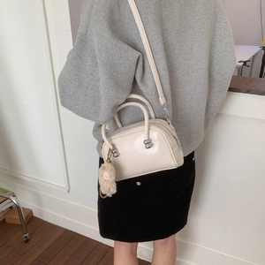 Détail d'un sac à bandoulière blanc crème brillant avec un charme en peluche sur modèle