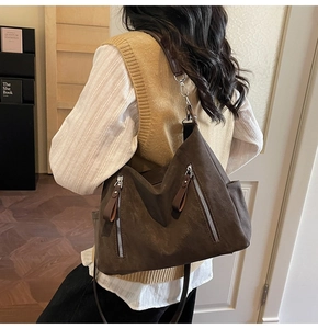 Detail of brown suede crossbody bag showing metal zippers and side pocket on model