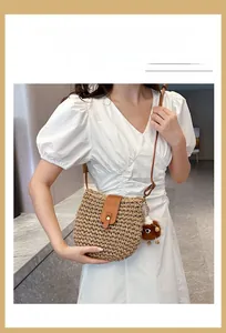 Detail of hand-woven straw crossbody bag with brown leather flap and plush charm