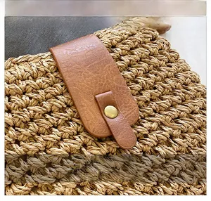 Detail of woven straw bag showing the texture, brown leather buckle and metal snap button
