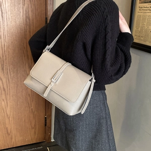 Detail of grey pebbled leather crossbody bag worn by a model in a minimal setting