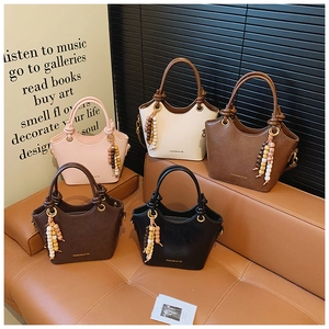 Detalle de cinco bolsos tote de cuero mate con asas anudadas y borlas de cuentas