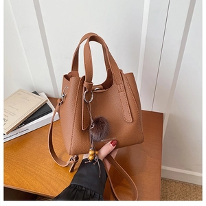 Détail du sac seau marron en cuir litchi avec pompon en fourrure et logo de marque