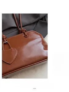 Detail of caramel leather handbag featuring knotted handle and heart-shaped charm accessory