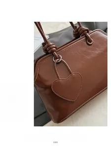 Detail of a brown tote bag with glossy faux leather texture and a heart-shaped charm