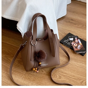 Détail d'un sac seau en cuir marron à motif litchi avec breloque boule en peluche