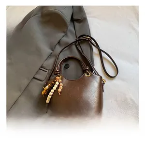 Detalle de bolso cubo marrón oscuro en cuero encerado con un colgante de cuentas decorativo