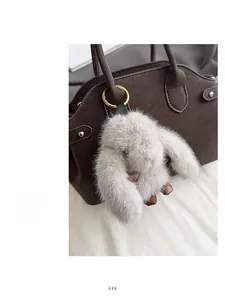 Close-up of a fluffy light grey rabbit charm on a brown textured leather baguette bag