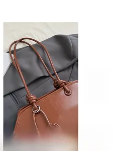 Detail of caramel brown leather tote featuring knotted shoulder straps and metallic hardware