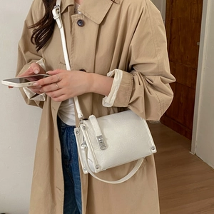 Close-up of white pleated leather bag with silver metal buckle and rivets on beige trench coat