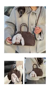 Brown faux leather shell handbag with plush rabbit charm shown on a grey coat model