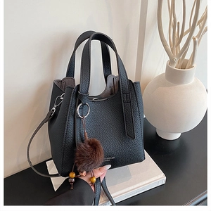 Détail du sac cabas noir grainé avec breloque en peluche sur fond de livre blanc