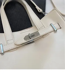 Detail of silver twist lock hardware and grain leather texture on beige square handbag