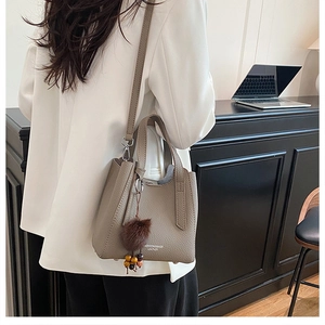 Détail d'un sac seau en cuir gris avec charme en peluche et bandoulière amovible