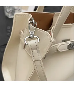 Detail of silver hardware hook and strap connection on a beige crossbody bag