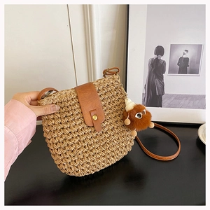 Detail of woven straw shoulder bag with brown leather flap and fluffy monster charm