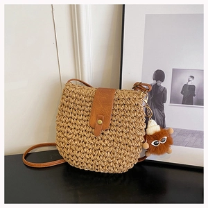 Detail of woven straw bag featuring a brown leather flap and cute monster plush charm
