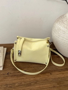 Chic light yellow leather boston pillow bag with adjustable strap on a wooden table