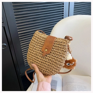 Close-up of woven straw crossbody bag with brown leather flap and stylish plush ball charm