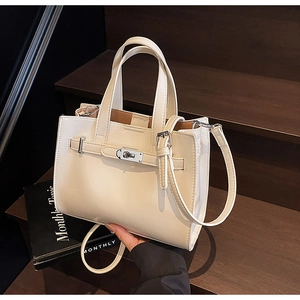 Detail of cream leather tote bag with metallic twist lock on dark wooden steps