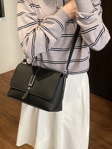 Minimalist black crossbody bag with silver buckle and pebbled leather texture on model
