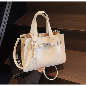 Detail view of cream leather tote bag with silver turn-lock and adjustable strap on wood